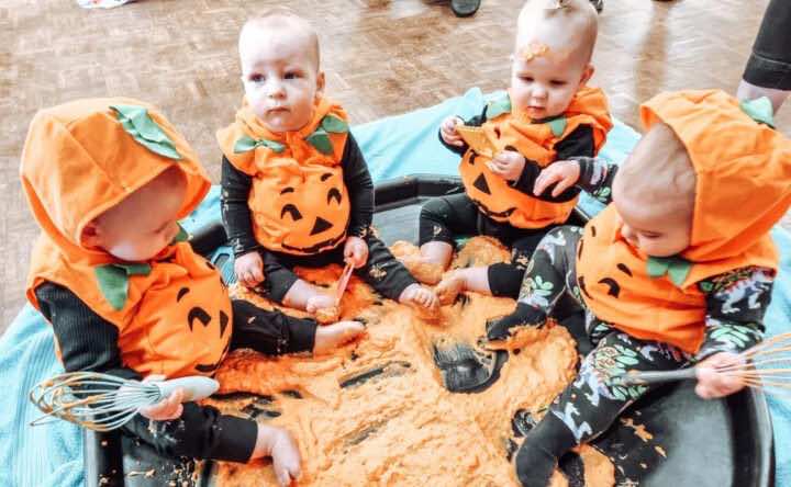 Little Learners dressed as pumpkins play in a messy play tray at a halloween messy play class