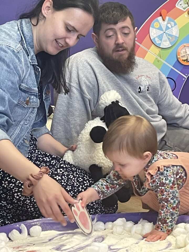 A mum, dad and baby play in a flour filled messy play tray